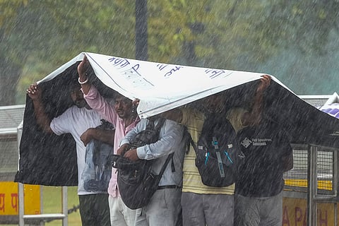 People take cover under a plastic sheet during heavy rainfall, in New Delhi, Thursday, Oct. 15, 2026. 