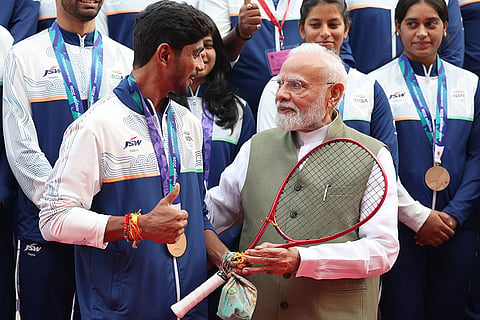 In this image posted on Oct. 15, 2026, Prime Minister Narendra Modi is presented a racquet by soft tennis player Jay Meena, who won a bronze medal, during an interaction with Asian Games 2026 medal winners at Major Dhyan Chand National Stadium, in New Delhi.