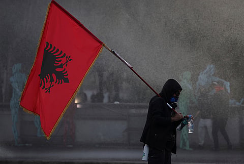 A hooded protester holding an Albanian flag is sprayed by a police water cannon during an anti-government demonstration in Tirana, Albania, Friday, Oct. 16, 2026. 
