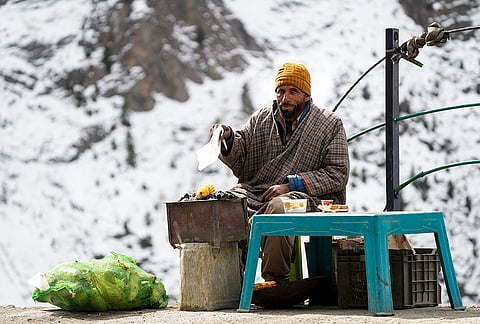 A vendor roasts corn over a charcoal stove along the Srinagar-Leh National Highway after a fresh spell of snowfall near Zojila Pass, in Jammu and Kashmir, Saturday, Oct. 17, 2026. 
