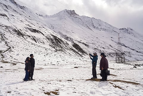 Tourists click photographs against the backdrop of snow-capped mountains following a fresh spell of snowfall near Zojila Pass along the Srinagar-Leh National Highway in Jammu and Kashmir, Saturday, Oct. 17, 2026. 