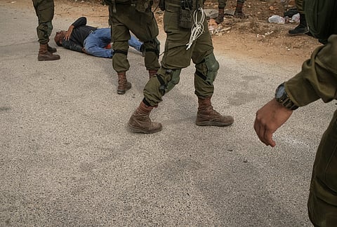 Israeli soldiers stand beside a wounded Palestinian man lying on a road after they shot him in the leg following a settler attack on Palestinians harvesting olives in the West Bank village of Abu Falah.