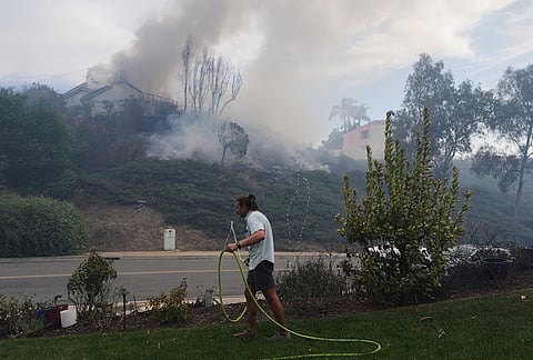 Resident Ephraim Taylor, grabs a garden hose in an effort to help with a wildfire spreading in his neighborhood, during the Norte Fire on Friday, Oct. 16, 2026, in San Juan Capistrano, California.
