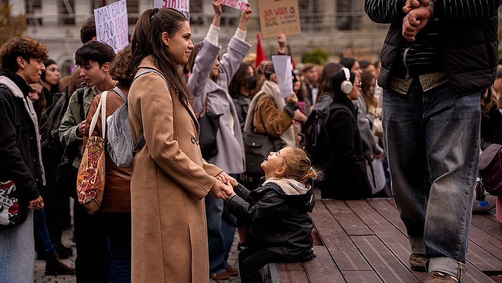 A woman holds hands with a child during a protest aiming to raise awareness to the violence and prejudice against women in Romanian society, in Bucharest, Romania, Saturday, Oct. 17, 2026. - | Photo: AP/Andreea Alexandru