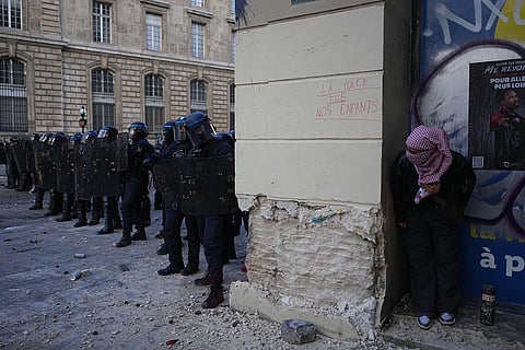 A protester watches riot police next to a tag reading 'Police kill our children' during a demonstration against rising living costs, joining students' grievances, in Paris, Saturday, Oct. 17, 2026.