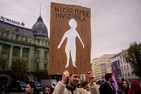A man holds a cutout reading "No woman is invisible" during a protest aiming to raise awareness to the violence and prejudice against women in Romanian society, in Bucharest, Romania, Saturday, Oct. 17, 2026.