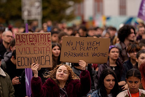 A woman hold placards reading "Austerity=Economic Violence" and "We don't want to pay for your wars" during a protest aiming to raise awareness to the violence and prejudice against women in Romanian society, in Bucharest, Romania, Saturday, Oct. 17, 2026.