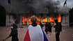 France’s Streets Fall Quiet Under Curfews, But Fresh Protests Loom | Photo: AP/Laurent Cipriani : A protester wraps a French flag around them in front of the burning tourism office during a demonstration against rising living costs and in solidarity with students’ grievances in Lyon, France, Saturday, Oct. 17, 2026.