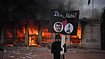 | Photo: AP/Laurent Cipriani : A protester holds a board with a photo of French president Emmanuel Macron in front of a burning tourism office during a demonstration against rising living costs and in solidarity with students’ grievances in Lyon, France