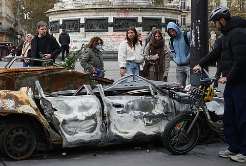 People watch a burned-out car after a quiet night Monday under curfew, the first since weekend protests over the cost of living turned into rioting and looting across France, in Paris, Tuesday, Oct. 20, 2026. 
