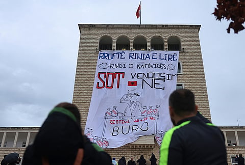 People watch at a large banner reading, in Albanian, "Long Live the Free Youth! Today We Decide. Prison for the System," hanging from the Polytechnic University during an anti-government protest in Tirana, Albania, Wednesday, Oct. 21, 2026. 