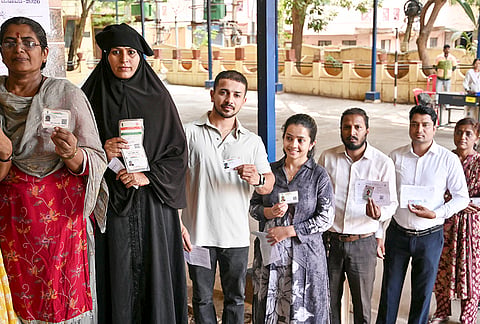 Voters show their identity cards as they wait in a queue outside a polling station to cast their votes for the West Graduates Constituency of the Karnataka Legislative Council elections, in Hubballi-Dharwad district.