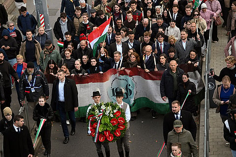 Hungarian Prime Minister Peter Magyar, center, waves a Hungarian flag with a hole cut in its middle, which symbolizes the Hungarian revolution in 1956, during the traditional torchlight memorial march of the 70th anniversary of the outbreak of the Hungarian Revolution and Freedom Fight of 1956 against Soviet oppression in Budapest, Hungary, Thursday, Oct. 22, 2026.