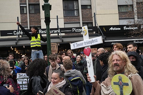 Protester holds a cross reading, “Love will triumph,” during a demonstration against rising living costs in Paris, Saturday, Oct. 24, 2026.