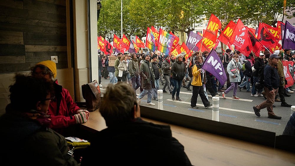 People sitting in a pub watch demonstrators during a protest on the sidelines of the far-right Rassemblement National (RN) congress in Orleans, France, Saturday, Oct. 24, 2026. - | Photo: AP/Teresa Suarez