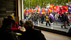 In Photos: Protests Sweep France As Rising Costs And Far-Right Politics Draw Crowds | Photo: AP/Teresa Suarez : People sitting in a pub watch demonstrators during a protest on the sidelines of the far-right Rassemblement National (RN) congress in Orleans, France, Saturday, Oct. 24, 2026.