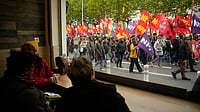 In Photos: Protests Sweep France As Rising Costs And Far-Right Politics Draw Crowds | Photo: AP/Teresa Suarez : People sitting in a pub watch demonstrators during a protest on the sidelines of the far-right Rassemblement National (RN) congress in Orleans, France, Saturday, Oct. 24, 2026.