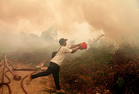 A man attempts to put out a wildfire burning through a field near a residential area in Palembang, South Sumatra, Indonesia, Friday, Oct. 23, 2026. 

