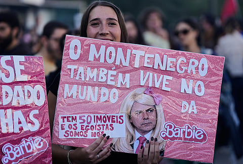 A woman holds a banner referring to Portugal’s Prime Minister Luis Montenegro during a protest to demand affordable housing in Lisbon on Saturday, Oct. 24, 2026. The test reads in Portuguese: "Montenegro also lives in Barbie world. He owns 50 properties, yet we're the selfish ones.". 
