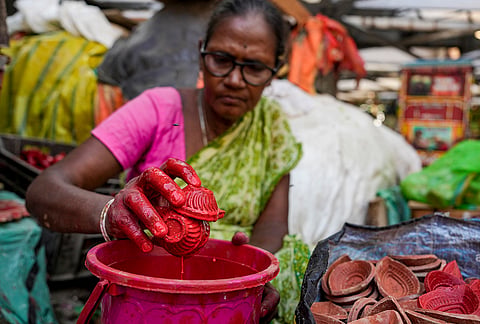 An artisan dips earthen lamps into paint for sale ahead of the ‘Diwali’ festival, in Kolkata, Sunday, Oct. 25, 2026. 
