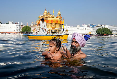 A man with a child take a holy dip in the 'sarovar' on the birth anniversary of Guru Ram Das, the fourth Sikh Guru, at the Golden Temple, in Amritsar, Punjab, Tuesday, Oct. 27, 2026. 