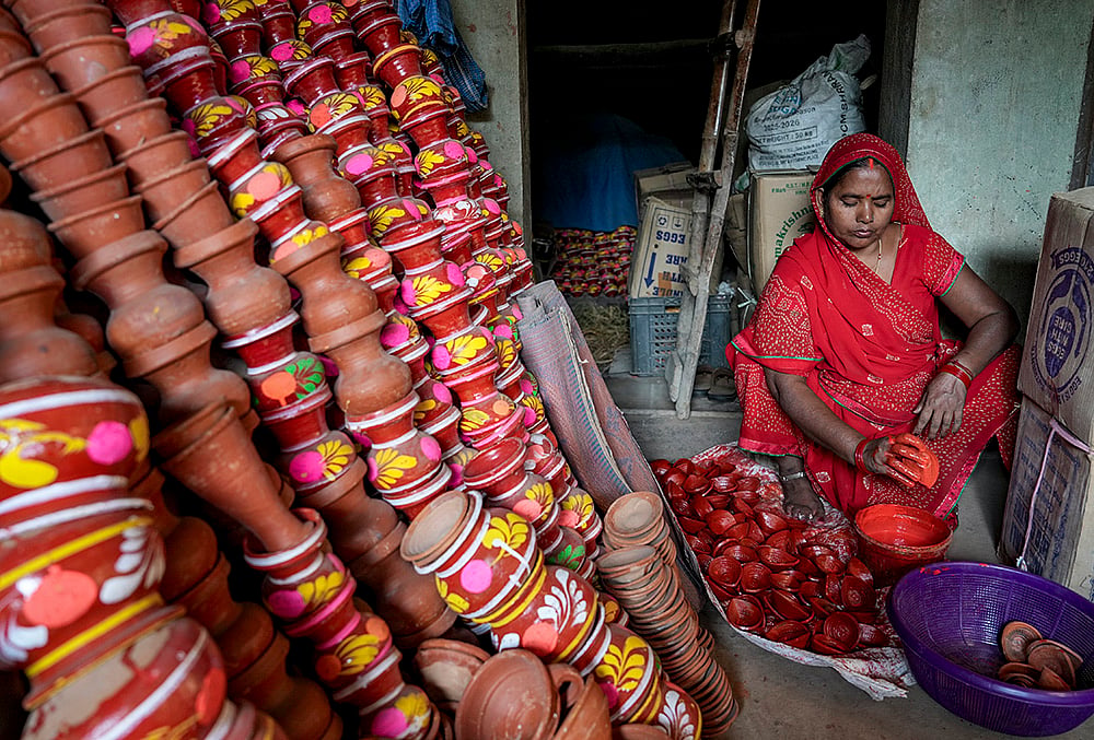 artisan dips an earthen lamp into paint for sale 