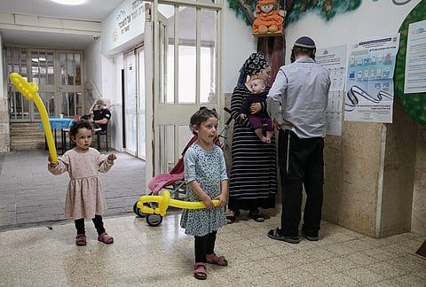 An Israeli settler couple check a voter list as their children hold balloons at a school used as a polling station during Israel's general election in the settlement of Kiryat Arba in the occupied West Bank, Tuesday, Oct. 27, 2026. 
