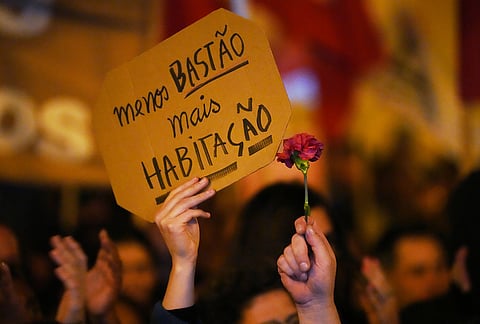 Protesters gather during a demonstration demanding affordable housing outside Portugal's Parliament in Lisbon, Tuesday, Oct. 27, 2026. The sign reads in Portuguese: "Less police, more housing." 
