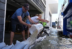| Photo: AP/Jae C. Hong : Members of the Deakins family remove floodwater from their garage in Huntington Beach, California, Wednesday, Oct. 28, 2026.