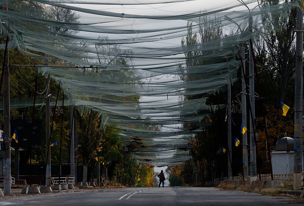 A woman walks beneath anti-drone nets stretched over a street during a local ceasefire related to a humanitarian aid mission in Oleshky, in Kherson, Ukraine, Wednesday, Oct. 28, 2026.  - | Photo: AP/Evgeniy Maloletka