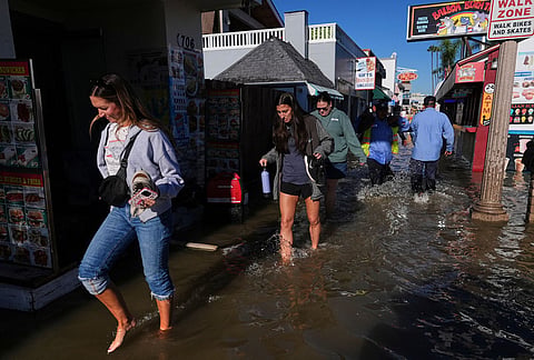 Tourists walk through floodwaters in Newport Beach, California., Monday, Oct. 26, 2026. 