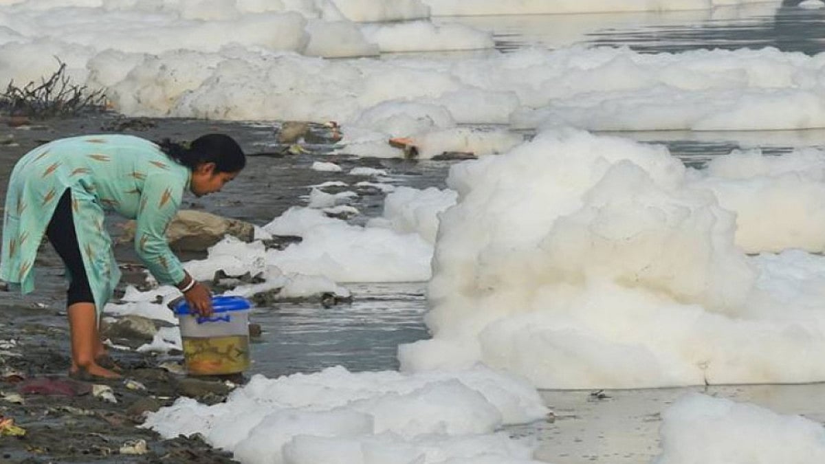 A woman shifts fishes in the Yamuna river while toxic foam floats at Kalindi Kunj, in New Delhi. 