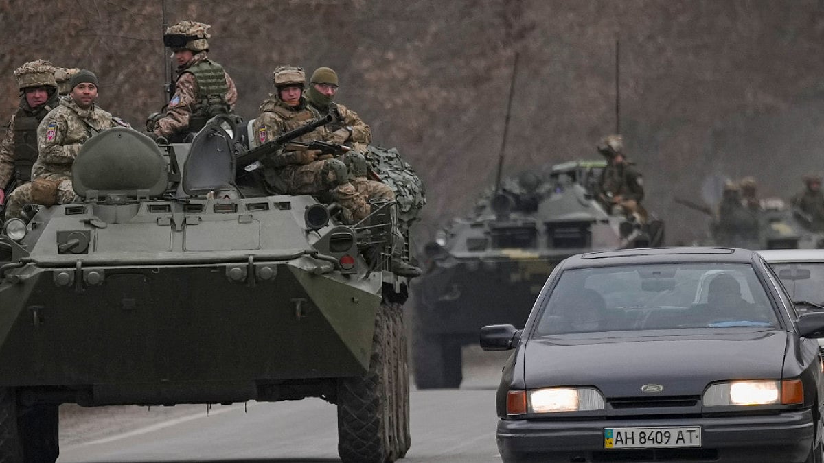 Ukrainian servicemen sit atop armored personnel carriers driving on a road in the Donetsk region