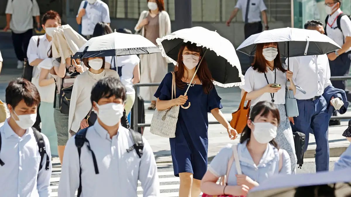 People holding parasols cross an intersection amid heat, in Tokyo