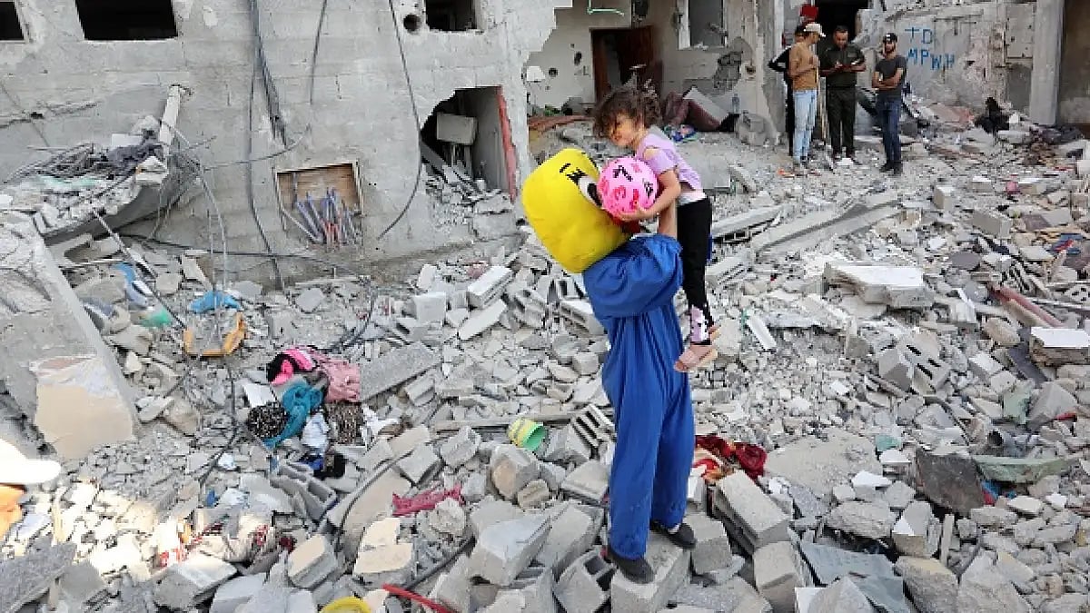 A Palestinian clown carries a child during a show amidst the rubble of a building destroyed in the latest round of fighting between Israel and Palestinian militants, in Rafah in the southern Gaza Strip on August 9, 2022.