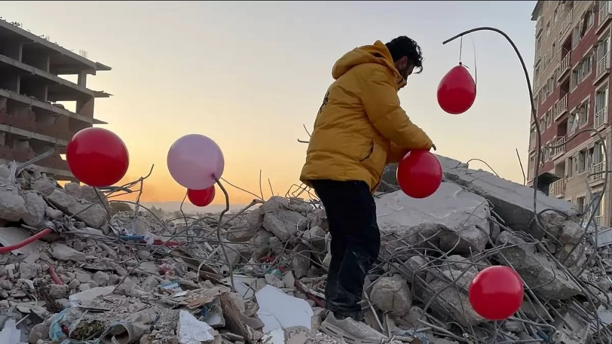 Ogun Sever Okur climbing atop debris to tie red balloons in memory of children