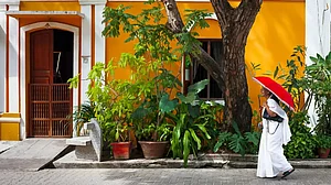 Indian woman in white sari walking by a colorful house in Pondicherry