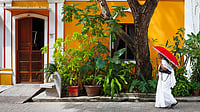 Short Story: When A Riotous Mohenambal Came To Stay With Akka... Indian woman in white sari walking by a colorful house in Pondicherry