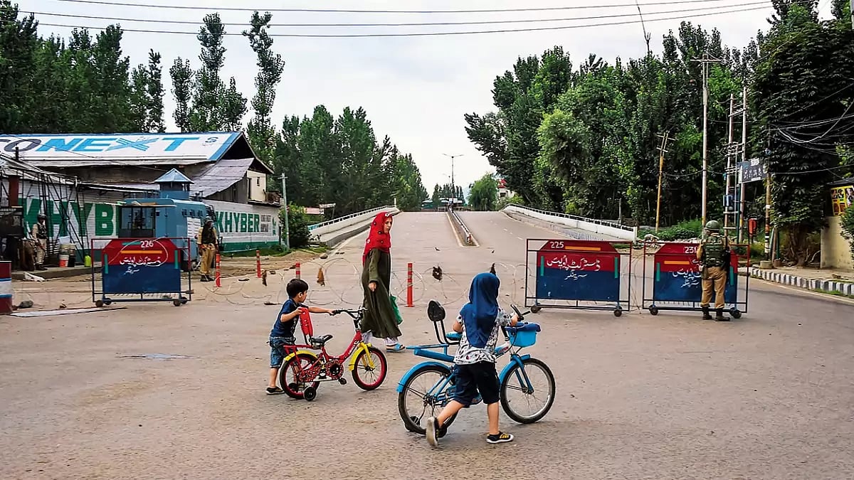 The Kashmir Life: A woman walks with her children as security personnel stand guard  - null