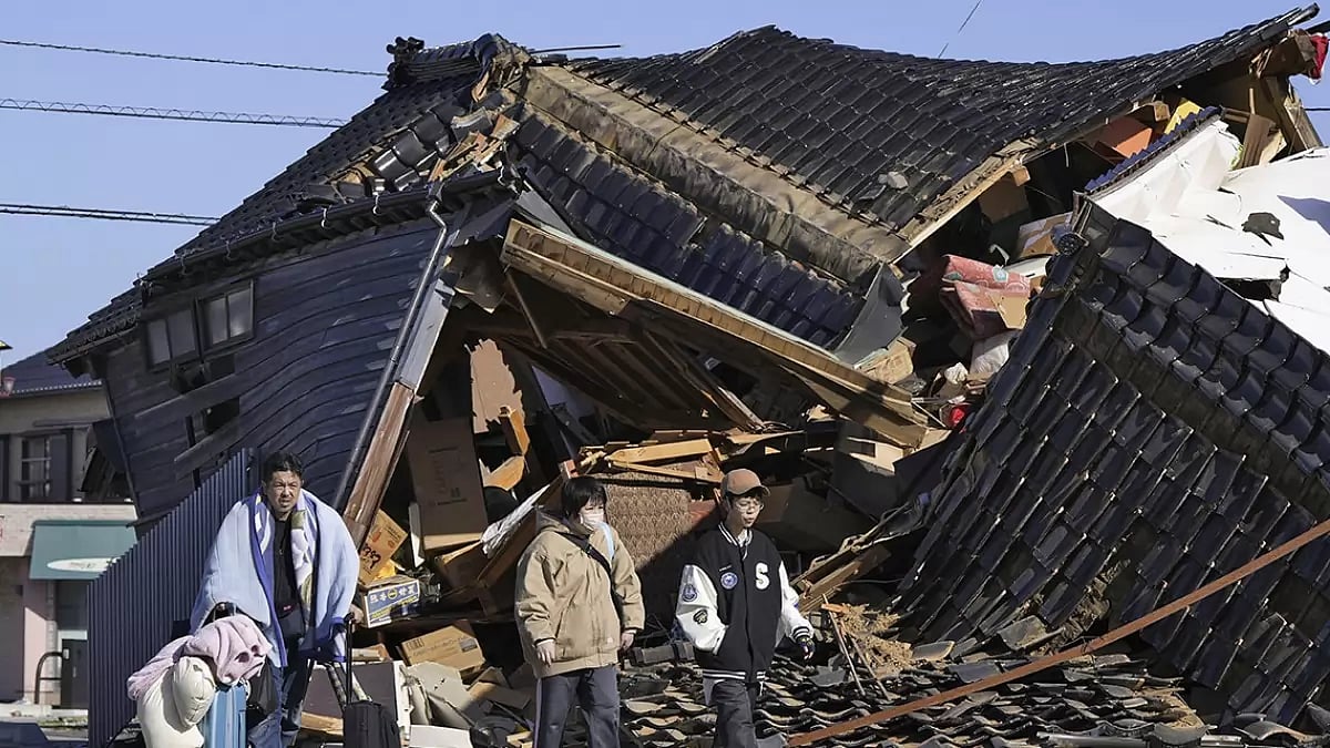 A man carries his belongings past a collapsed house 