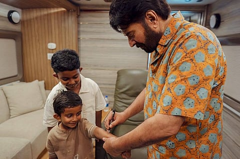 റോബർട്ട് കുര്യാക്കോസിന്റെ ഇളയ മകൻ ഇമ്മാനുവലിന്റെ ദേഹത്ത് ഓട്ടോ​ഗ്രാഫ് നല്കുന്ന മമ്മൂട്ടി. മൂത്തമകൻ നോവ സമീപം 
