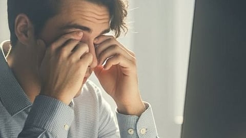 A stressed person holding a smartphone and rubbing tired eyes due to high screen time"