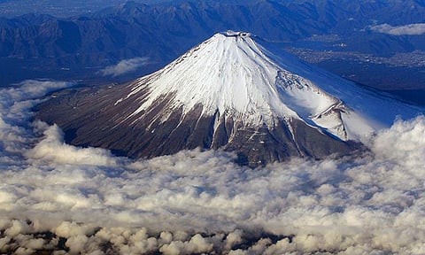 In this Dec. 8, 2010 file photo, snow-covered Mount Fuji, Japan's highest peak at 3,776-meters tall (12,385 feet), is seen from an airplane window. Those who want to climb one of the most popular trails of the iconic Japanese Mount Fuji will now have to reserve ahead and pay a fee as the picturesque stratovolcano struggles with overtourism, littering and those who attempt rushed “bullet climbing,” putting lives at risk. 