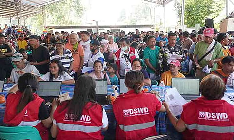 FILIPINO AID PAYOUT. Department of Social Welfare and Development (DSWD) personnel verify digital records and process cash assistance for local beneficiaries at an indoor deployment site in the Philippines, facilitating efficient data matching to streamline social protection services.