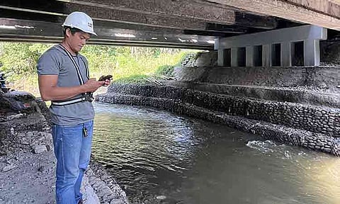 A man checks his mobile device while inspecting a flood-control structure beneath a bridge in the Philippines. Digital field monitoring can help project teams track progress and identify potential delays.