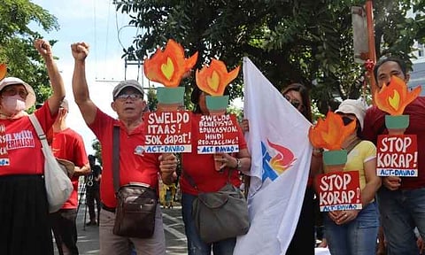 Protesters from the Alliance of Concerned Teachers (ACT) Davao raise their fists and hold creative flame-shaped placards during a street demonstration demanding higher wages and an end to corruption. The placards call for a 50,000 PHP minimum monthly salary ("Sweldo Itaas! 50k Dapat!") and urge an end to "red-tagging" and government corruption ("Stop Korap!").