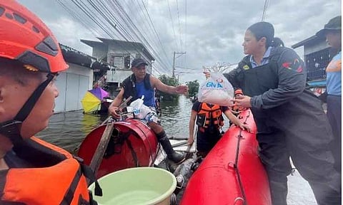 A volunteer from the GMA Kapuso Foundation hands over a relief pack to a resident navigating a heavily flooded street on a makeshift drum raft in San Simon, Pampanga, Philippines. The relief distribution, held as part of the foundation's "Operation Bayanihan," delivered food packs, hygiene kits, and essential supplies to hundreds of families displaced by relentless flooding caused by the enhanced southwest monsoon (habagat) rains.