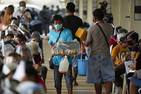 MANILA. Vendors sell food and water to waiting residents at a vaccination center in Quezon City on Sept. 13, 2021. (AP)
