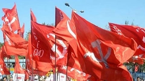 Red flags of the Communist Party of India (Marxist) bearing the sickle, hammer, and star emblem. The flags appear to be held by workers at a rally