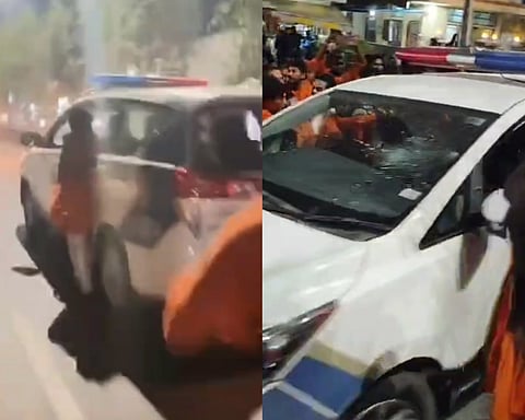 A man in Hanuman mala hanging on to the patrol car (on the left), a partially destroyed windscreen of patrol car
